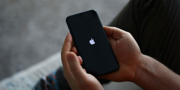 Tbilisi, Georgia - September 26, 2023: Person holds modern apple smartphone in hand. Apple logo burns on black screen of phone